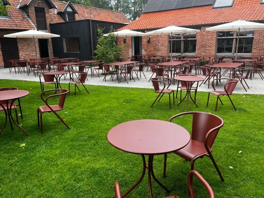 Slunečníky Nata nad stolky venkovní restaurace na travnatém dvoře